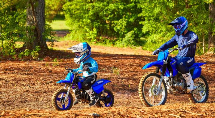 Image of father and son riding on their dirt bike with trees at their back.