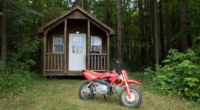 Image of Honda CRF50F dirt bike in the middle of the woods with wooden house at the back.