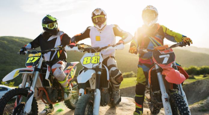 3 men sitting on their own dirt bike with a bright sun on their back