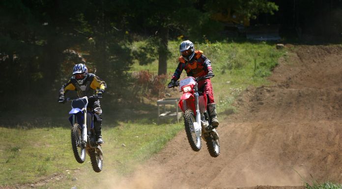 2 men jumping off their dirt bike in the trail
